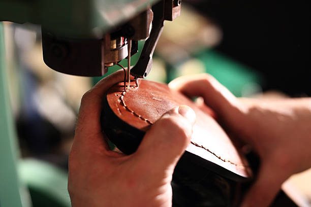 A cobbler hand-stitches a leather shoe sole on a sewing machine